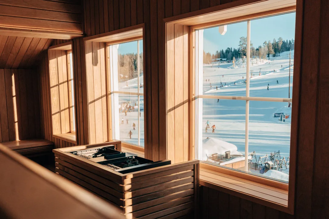 Vyn från bastun fönster. Utanför ser man skidbacken där skidgäster svänger i backen.
