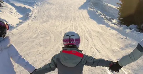 Tre skidåkande tjejer håller varandra i handen när det åker skidor ner ör Lämmeltåget