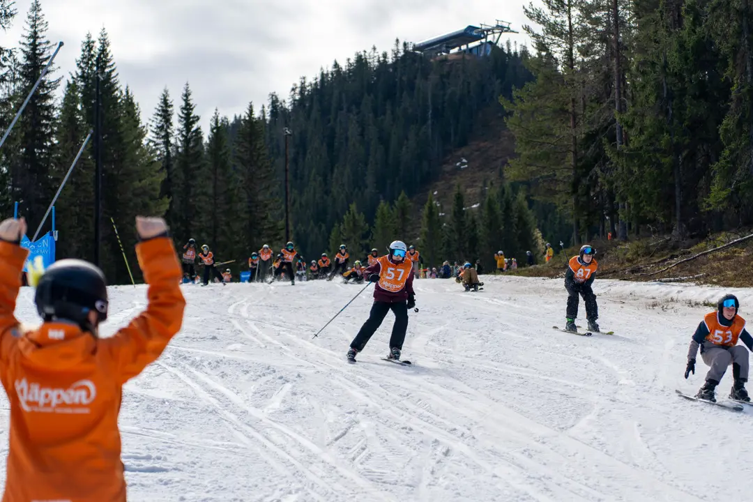 The ski instructor is cheering on all the children coming down in the Chinese Easter Downhill race.