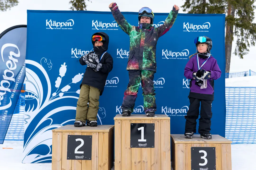 Happy snowboarders standing on the podium, with the winner cheering and raising their hands in the air.