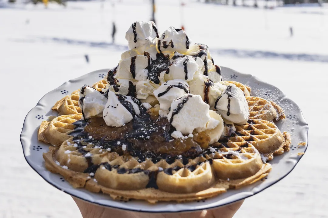 En bild på en våffla toppad med grädde, maränger och chokladsås